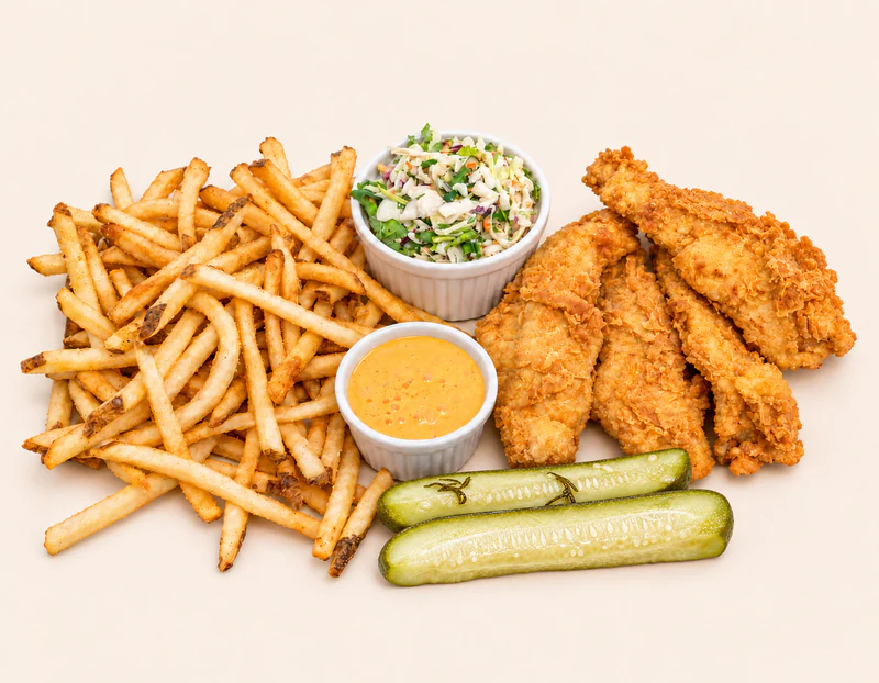 Four golden chicken tenders with fries, coleslaw, sauce, and homemade pickle spears